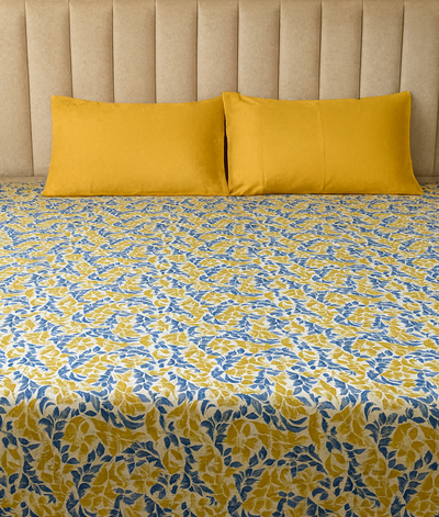 Bed with yellow and blue patterned bedding and two yellow pillows against a beige headboard.