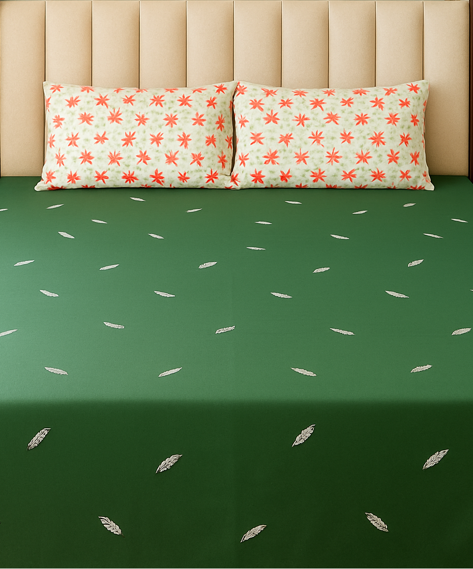 Green bedspread with white patterns on a bed with floral-patterned pillows.