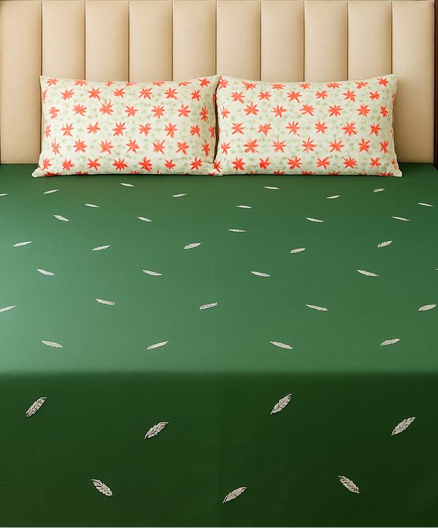 Green bedspread with white patterns on a bed with floral-patterned pillows.